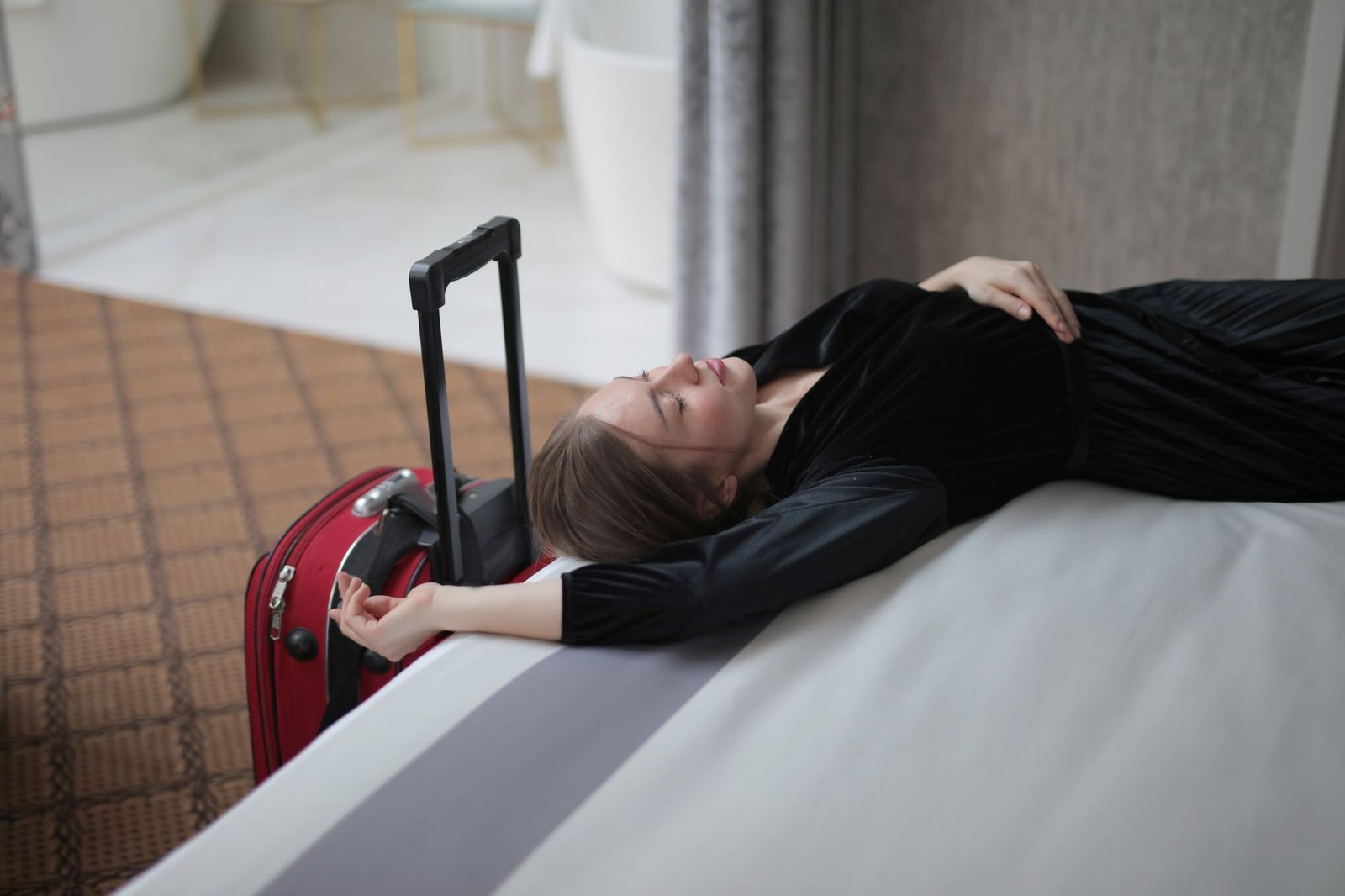 Voyageuse allongée sur un lit d’hôtel avec sa valise après un long trajet pour illustrer la fatigue liée au jet lag