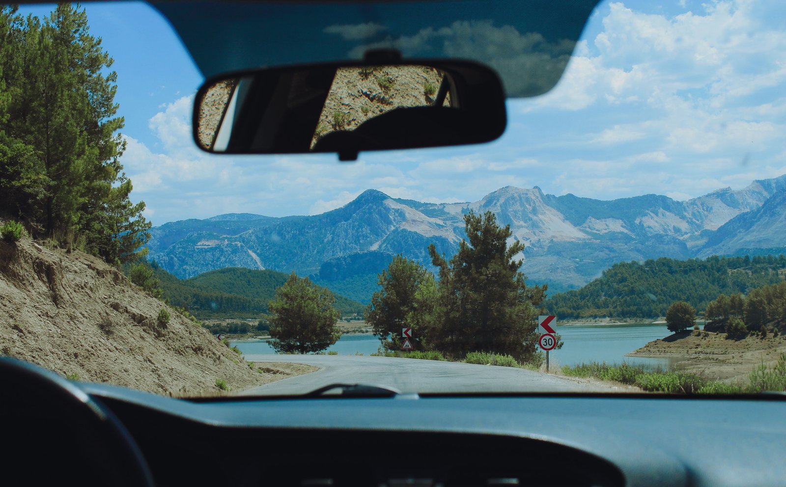 Vue depuis l’intérieur d’une voiture sur une route de montagne pour illustrer la liberté d’une location de voiture en voyage